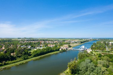 Pegasus Köprüsü 'nün çevresindeki yeşil ağaçlardan, köy evlerinden ve Normandiya' daki canlı mavi gökyüzünün altındaki açık arazilerden oluşan sakin bir nehri geçerken geniş bir hava perspektifi..