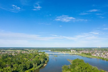 Geniş hava manzarası, Loire Nehri 'nin Sully-sur-Loire' den geçtiğini, yeşil nehir kıyılarıyla kasabayı açık mavi bir gökyüzü altında birleştirdiğini gösteriyor. Sahne açık, parlak ve bereketli bitki örtüsüyle huzur dolu..