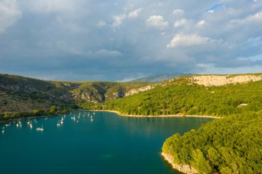 Bauduen yakınlarındaki sık orman ve dramatik kireçtaşı kayalıklarıyla çevrili turkuaz sularda demirli yelkenlilerin bulunduğu sessiz bir körfezin havadan görünüşü kasvetli bir gökyüzünün altında..