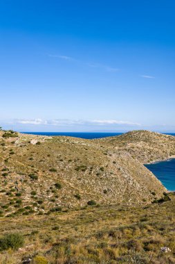 Kuru otlarla kaplı yuvarlanan kayalık tepeler Yunanistan 'ın Cap Tenare kentindeki canlı mavi Akdeniz' e doğru iniyor. Açık arazi, uçsuz bucaksız, berrak bir gökyüzünün altında parlak güneş ışığıyla yıkanır. Huzur ve doğal güzelliği çağrıştırır..
