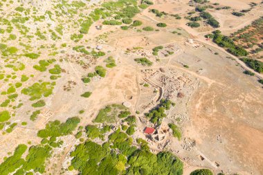Girit 'in eski Falasarna limanındaki yeşil bitki örtüsü parçalarıyla güneşli, kurak bir araziye yayılmış arkeolojik kalıntıların havadan görünüşü. Sahne tarih, açıklık ve engebeli Akdeniz dokularını aktarıyor.