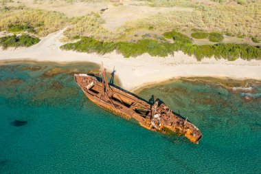 Paslanmış Dimitrios gemi enkazının insansız hava aracı perspektifi Gythio yakınlarındaki kumlu bir sahil şeridi boyunca berrak turkuaz sularda dinleniyor. Etrafı vahşi bitki örtüsü ve güneş ışığıyla çevrili kıyı dokularıyla çevrili..