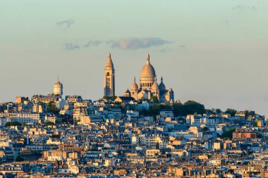 İkonik Sacre Coeur Bazilikası Montmartre 'ın yoğun çatılarının üzerinde yükselir, sıcak altın gün batımı ışığı altında yumuşak pastel gökyüzü ile yıkanır..