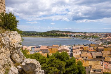 Büyük kireçtaşı kayaları turuncu kiremitli köy çatıları ve Gruissan 'da parıldayan bir göl üzerinde panoramik bir manzara oluşturuyor. Güneş ışığı ve dağınık bulutlar arazi ve su boyunca dinamik gölgeler yaratır..