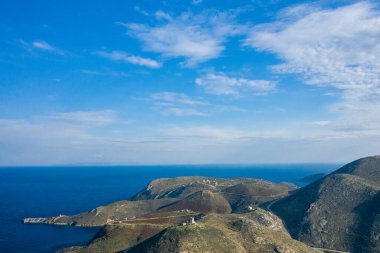 Engebeli tepelerin havadan görünüşü ve Yunanistan 'ın Magne kentinde engin mavi Akdeniz' le çarpıcı bir kıyı şeridi buluşması. İnce bulutlar parlak bir gökyüzünde sürükleniyor, desenli arazide yumuşak gölgeler bırakıyor..