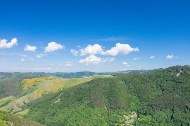 Bereketli yeşil tepelerin ve açık mavi gökyüzünün altındaki yoğun ormanların geniş hava manzarası Ardeche kırsalında dağınık beyaz bulutlar..