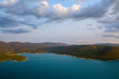 Lac de Sainte-Croix eğrisinin geniş turkuaz suları yumuşak akşam bulutları ve yumuşak ışıkla dolu bir gökyüzünün altındaki ormanlık tepeler boyunca uzanır..