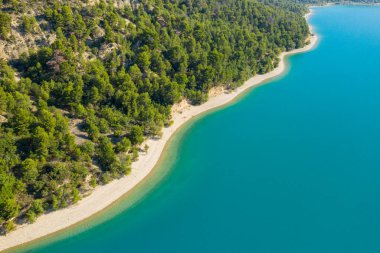 Çam ağacıyla kaplı bir yamacın havadan görünüşü Provence 'de güneşli bir günde turkuaz su ve kumlu kıyı kenarını karşılıyor..
