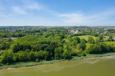 Sakin bir nehir kıyısı boyunca uzanan yoğun yeşil ormanın havadan görünüşü. Küçük bir köy ve parlak mavi gökyüzünün altında açık alanlar..