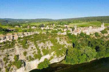 Aigueze 'nin panoramik hava manzarası kireçtaşı kayalıklara tünemiş, yeşil vadi ve nehir manzaralı kilise kuleleri açık bir yaz gününde.