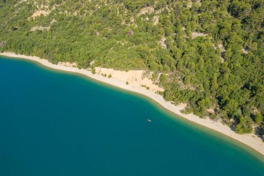 Lac de Sainte-Croix 'in kumlu kıvrımlarında yüzen tek bir kanonun havadan görünüşü yoğun yeşil orman ve parlak güneş ışığı altındaki canlı mavi sularla çevrili..