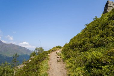 Pireneler 'in dağlarındaki verimli bir yamaç boyunca uzanan güneşli toprak bir patika yoğun yeşillik ve uzak tepelerle çevrili açık bir gökyüzü..