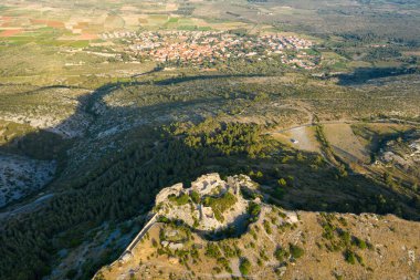 Antik taş şatonun havadan bakış açısı engebeli bir tepenin üzerinde, uzak bir köy ve altın güneş ışığıyla yıkanmış yamalı tarlalarla çevrili bir çam ağacı ve yabani bitki örtüsü ile yıkanıyor..