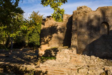 Yunanistan 'ın Olympia kentindeki Nero Villası' nın antik tuğla duvarları sıcak öğleden sonra güneşiyle aydınlatılıyor ve olgun ağaçlarla çevrili. Dokulu duvar ustası ve yapraklı gölgeler bu tarihi arkeolojik alanda sakin bir atmosfer yaratıyor..