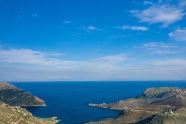 Yunanistan 'ın Magne kentinde sakin mavi Akdeniz' le buluşan engebeli tepelerin geniş hava manzarası. Sahnede bulutlar dağılmış ve kıyı arazisi aydınlık gün ışığı altında berrak gökyüzü yer alıyor..