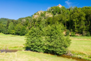 Kırmızı çatılı ıssız bir ev kayalık bir tepenin üzerinde, sık yeşil ormanlara tepeden bakan ve Morvan kırsalında dolambaçlı bir deresi olan güneşli bir çayır. Sahne berrak mavi gökyüzünün altında dingin ve dingin..