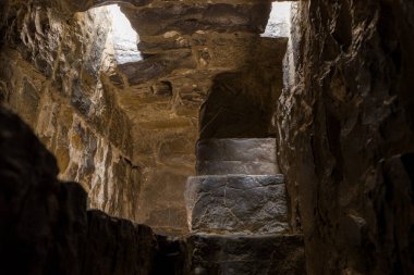 Aşınmış taş basamaklar, yukarıdaki bir açıklıktan süzülen doğal ışıkla, ortaçağ kulesinin dar ve loş bir geçidi içinde yükselir. Sert dokular ve gölgeler, tarihi mimarinin yaşını ve gizemini vurgular..