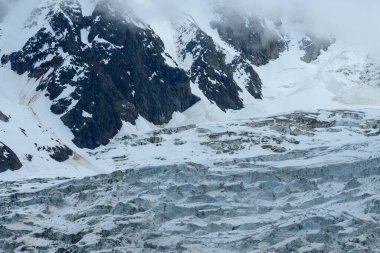 Kırık mavi Buzul des Bossons buzu, Fransız Alpleri 'ndeki sarp, karla kaplı kaya yüzeyleri ve alçak bulutlarla tezat oluşturarak dramatik ve engebeli bir dağ manzarası yaratır..