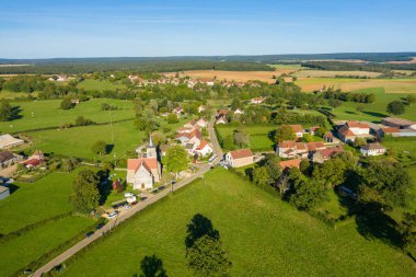 Fransa 'nın Burgundy kentindeki açık mavi gökyüzü altında tarihi taştan kilisesi, kırmızı çatıları ve yemyeşil çayırları olan Sakar Köyü' nün yüksek açılı manzarası..