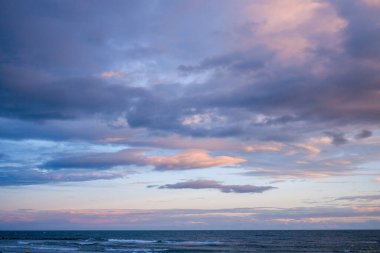 Agde yakınlarındaki sakin Akdeniz 'in üzerinde pembe ve mavi renkte canlı pastel bulutlar. Yumuşak akşam ışığı huzurlu ve atmosferik bir kıyı manzarası yaratır..