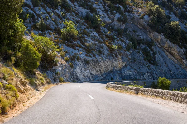 Taştan bir duvarla çevrili boş virajlı yol, güneşli kayalık yamaçlar boyunca kıvrılıyor ve Alpes-de-Haute-Provence 'deki seyrek bitki örtüsü.