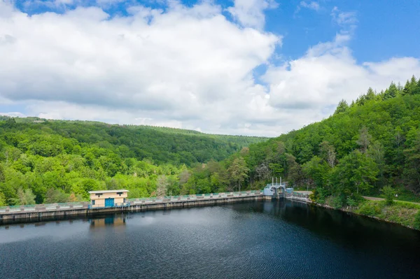 Sakin bir gölü çevreleyen beton bir barajın üzerinde küçük bir kamu binası duruyor. Etrafı yoğun yeşil ormanlarla çevrili ve Chaumecon gölündeki bulutlu mavi gökyüzünün altında yuvarlanan tepeler..