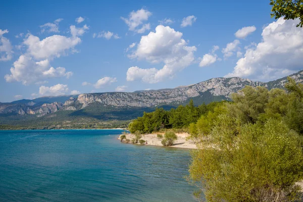 Bereketli yeşil bir yarımada, uzak engebeli dağlarla çevrili Sainte-Croix Gölü 'nün berrak mavi sularına ve kabarık beyaz bulutlarla dolu bir gökyüzüne çıkar..