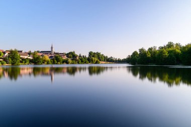 Aynaya benzeyen su, Dampierre en Burlys 'in kilise kulesinin ve sabah gökyüzünün altında yoğun yeşil ağaçlarla çevrili köy çatılarının yansımasını yakalar. Yumuşak ışık ve pürüzsüz yüzey dinginliği ve ferahlığı çağrıştırıyor..