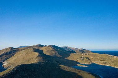 Yunanistan 'ın Cap Tenare kentindeki korunaklı bir körfeze inen güneşli dağ sırtlarının hava perspektifi. Açık mavi gökyüzü ve engebeli arazi uçsuz bucaksız bir yalnızlık hissi uyandırıyor..