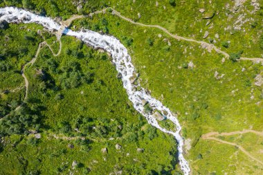 Hızlı akan bir nehrin yukarıdan aşağıya drone görüntüsü yemyeşil yamaçlarda süzülen kayalık arazi ve Pyrenean kırsalında kesişen yürüyüş yolları..