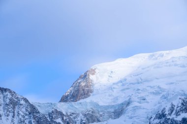 Yumuşak sabah ışığı, Mont Blanc du Tacul 'un buzlu yamaçlarını ve engebeli kayalarını aydınlatmakta. Kıtır kıtır kar ve sakin mavi gökyüzü, huzurlu bir alp atmosferi yaratmaktadır..