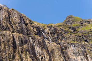 Gavarnie Sirki 'ndeki kayalık kayalıklar berrak mavi bir gökyüzünün altında yükseliyor. Engebeli, çizgili taşlardan akan şelaleler ve dramatik manzarayı şekillendiren yeşil yosun parçaları..