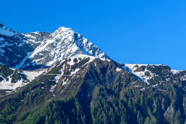 Mont Lachat sert bir kaya karışımı ile yükselir, bahar karı, ve yeşil orman canlı mavi bir gökyüzü altında. Gıcır gıcır güneş ışığı dağların çarpıcı dokularını ve zıtlıklarını vurgular..