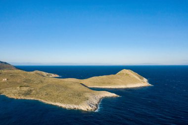 Yunanistan 'ın Cap Tenare kentindeki canlı mavi Akdeniz sularıyla çevrili rüzgarlı bir pelerinin havadan görünüşü. Açık gökyüzü ve engebeli kıyı şeridi çarpıcı bir izolasyon ve doğal güzellik hissi yaratır..