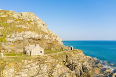 Cap de Carteret 'teki canlı mavi denize bakan dramatik uçurumların üzerinde ıssız bir taş bina duruyor. Kayalık arazi altın güneş ışığıyla aydınlatılır. Güçlü dokular ve uzak ve huzurlu bir atmosfer yaratır..