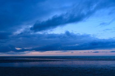 Huysuz alacakaranlık bulutları gökyüzünde İngiliz Kanalı 'nın sakin, yansıtıcı sularının üzerinde yumuşak mavi ve pembe renkler alçak gelgitte sakin bir deniz manzarası oluşturur..