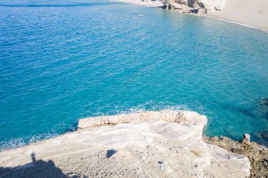 Güneş ışığıyla aydınlanan kireçtaşı, Girit 'in engebeli güney kıyısında canlı turkuaz suları ve kumlu bir koyu gözden kaçırır. Sahne parlak ve sakin, doğal dokuları ve kıyı berraklığını vurguluyor..