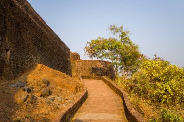 Kerala 'daki Bekal Kalesi' nde antik kale duvarları ve kuru bitki örtüsüyle çevrili taş kaldırım. Sıcak öğleden sonra ışığı, dokulu ve dünyevi tonları vurgular..