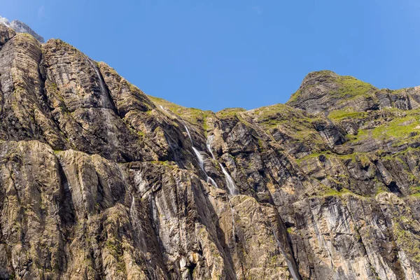 Gavarnie Sirki 'ndeki kayalık kayalıklar berrak mavi bir gökyüzünün altında yükseliyor. Engebeli, çizgili taşlardan akan şelaleler ve dramatik manzarayı şekillendiren yeşil yosun parçaları..