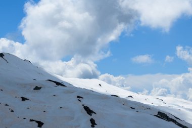 Rahatsız edilmemiş kar örtüsü Aiguillette des Houches 'ın yumuşak yamaçlarında dramatik kümülüs bulutları açık mavi gökyüzünde sürükleniyor ve beyaz manzaradan ortaya çıkan ince kaya çıkıntıları..