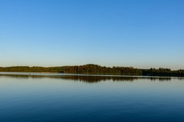 Settons Gölü 'nün durgun suları berrak mavi gökyüzünün altındaki yemyeşil ormanı yansıtır. Sakin ve sakin bir atmosfer için sabahın erken saatlerinde yumuşak bir ışıkla yıkanır..
