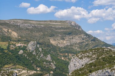 Verdon Vadisi 'ndeki küçük bir yamaçtan yükselen engebeli bir kireçtaşı platosunun geniş bir manzarası var. Yeşil vadileri ve dağınık bulutları parlak mavi gökyüzü altında..