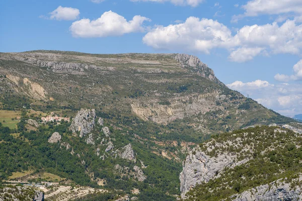 Verdon Vadisi 'ndeki küçük bir yamaçtan yükselen engebeli bir kireçtaşı platosunun geniş bir manzarası var. Yeşil vadileri ve dağınık bulutları parlak mavi gökyüzü altında..