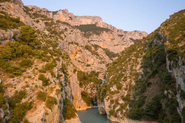 Sıcak bir akşam güneşi, engebeli kireçtaşı uçurumlarına ve Verdon Boğazı 'ndaki kıvrımlı nehrin üzerindeki yeşil bitki örtüsüne altın bir parıltı saçar..
