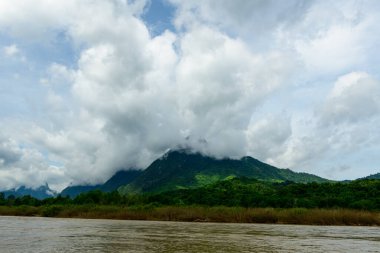Kuzey Laos 'taki Muang Ngoi yakınlarındaki Nam Ou Nehri' nin üzerindeki yemyeşil bir dağın üzerine yoğun beyaz bulutlar iner. Sahnede sık bir orman, çamurlu bir nehir kıyısı ve çarpıcı bir gökyüzü var. Dokunulmamış bir vahşi yaşam hissi yaratıyor..