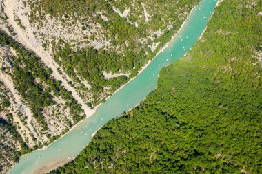 Dik kireçtaşı yamaçlar ve yoğun yeşil orman arasında kıvrılan canlı bir turkuaz nehrin yukarıdan aşağıya doğru görüntüsü güneşli bir yaz gününde Verdon Vadisi 'nde küçük teknelerle benekli..