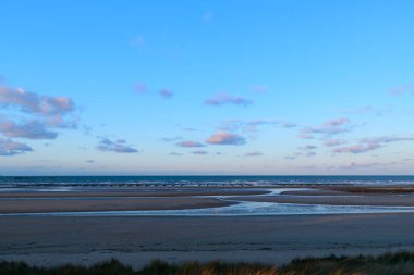 Utah Sahili 'nin geniş bir manzarası pürüzsüz kum, sığ gel-git havuzları ve dağınık bulutlu pastel bir gökyüzünün altında yumuşak bir sabah ışığı barındırır. Huzurlu kıyı manzarası sakin ve açık alanı çağrıştırıyor..