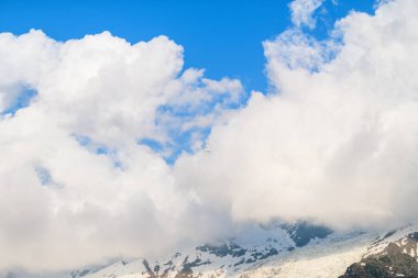 Geniş beyaz bulutlar Aiguille du Midi yakınlarındaki açık kayalarla kaplı karla kaplı bir dağ sırtı üzerinde sürükleniyor. Sahne Fransız Alpleri 'nde tazelik ve yükseliş gösteriyor..