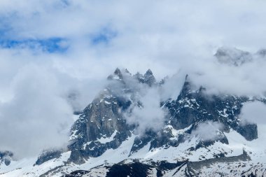Aiguille de Blaitiere 'in keskin kayalık zirveleri, Fransız Alpleri' nde devam eden kar ve dramatik dokularla sürüklenen bulutların arasından yükselir..