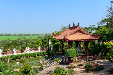 Manikürlü çalılarla çevrili kırmızı çatılı ahşap pavyon ve açık mavi gökyüzü altında yemyeşil kırlara bakan bir nilüfer göleti. Huzurlu bahçe, huzurlu bir ortamda heykel ve canlı yapraklar içeriyor..